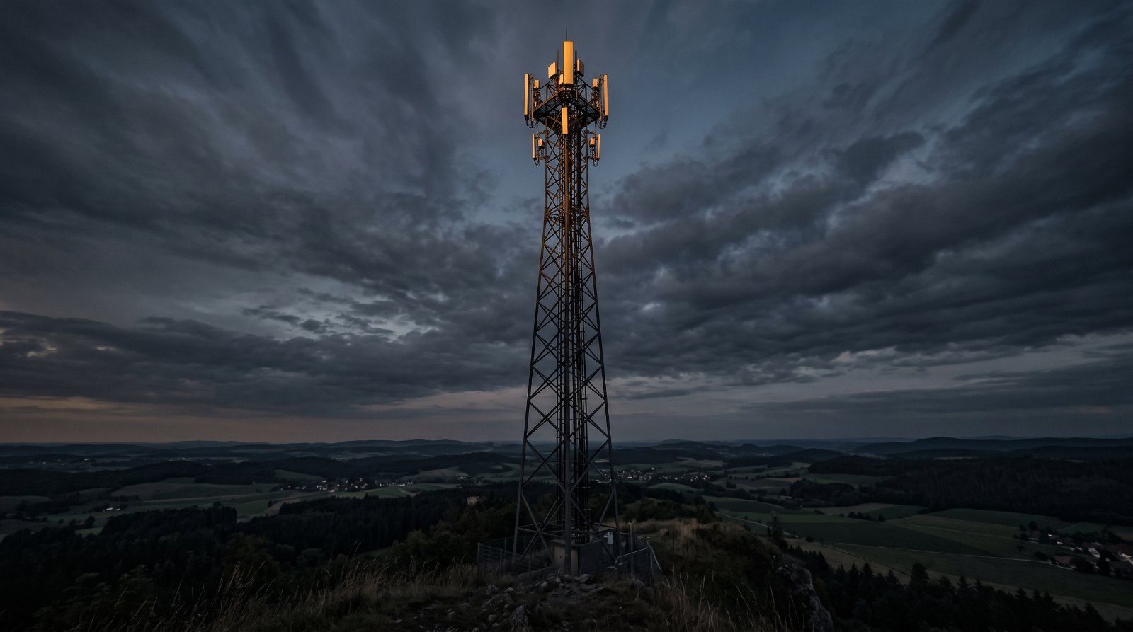 Mobilfunkmast in der Dämmerung über einer Mittelgebirgslandschaft